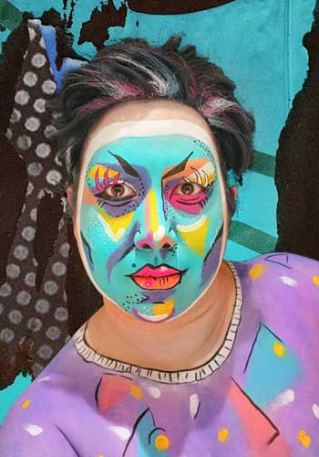 Image: Caine Panik – Self-portrait with very intense makeup in bright colors like an abstract modern painting, underlining the facial contours.