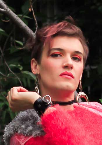 Image: Brigitte Oytoy with a look from below in pink red make-up and furry outfit, with large silver earrings.
